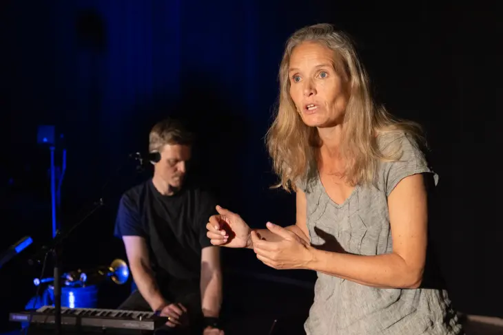 Engasjert dame som står foran en keyboardist og forteller en historie