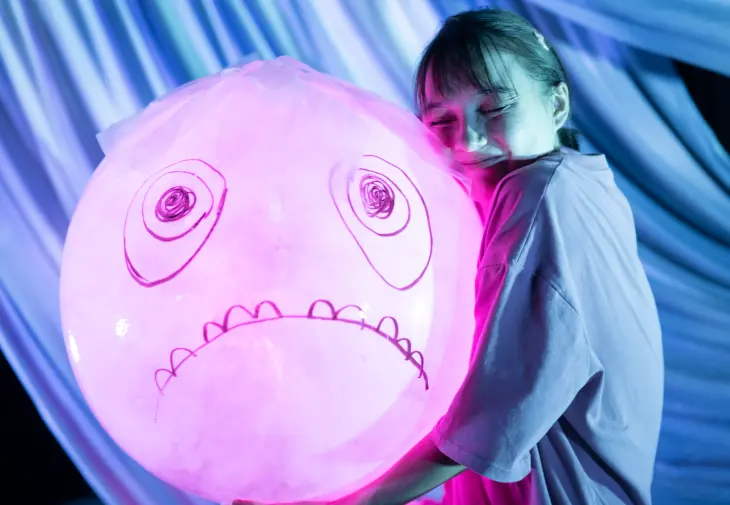 Smilende jente som holder stor ballong med påtegnet ansikt